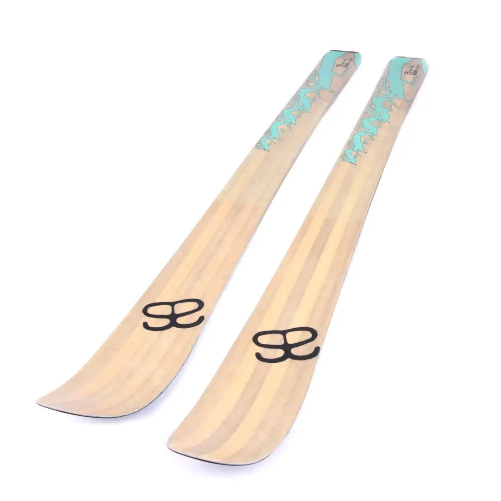 A pair of altai kom 150cm skis in light wood tone with subtle teal wave design and black logo branding