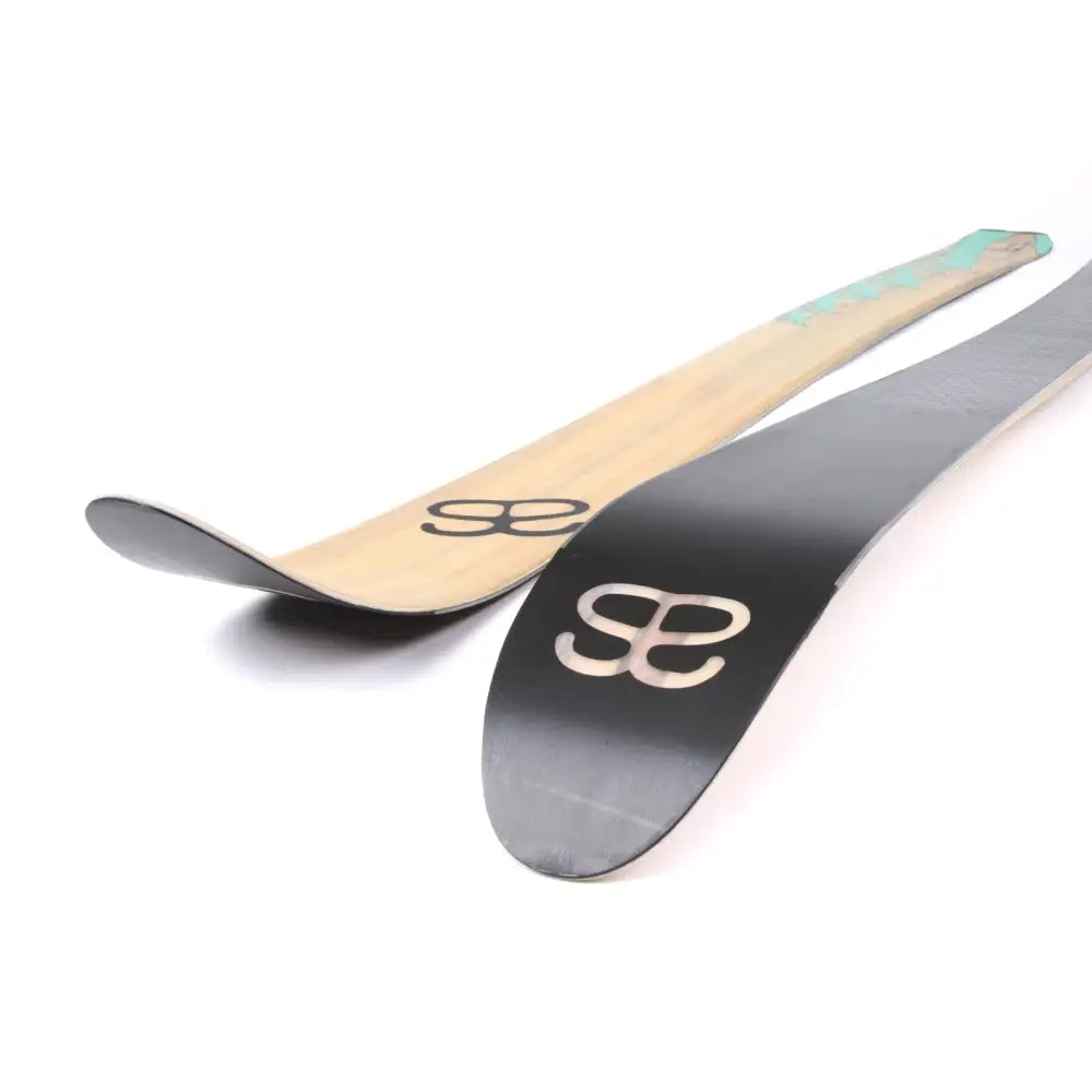 A pair of altai kom 150cm skis with one bamboo finish and one matte black surface both featuring silver logo decals