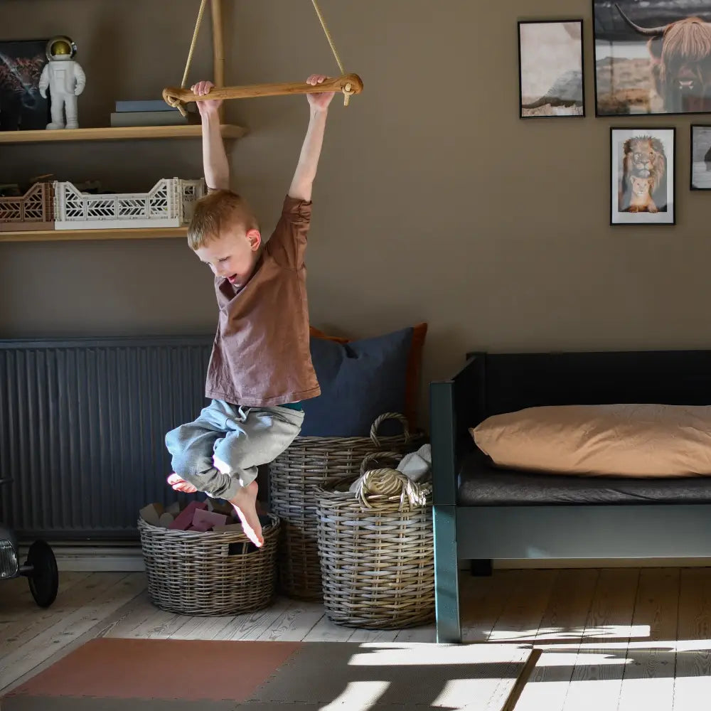 A child hanging from a bone oak beige wooden monkey bar with rope suspension in a cozy neutral room