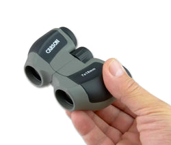 Gray and black carson miniscout 7x18mm pienikokoiset kiikarit kädessä esitettynä