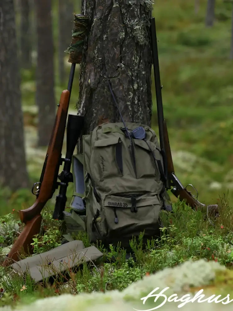 Olive green tactical backpack qunha 35 resting against tree in forest for outdoor use haghus korpimäki 35 päivärinkka asepussilla