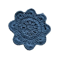 A hand-crocheted lasinalunen coaster in deep blue with a scalloped edge and textured pattern