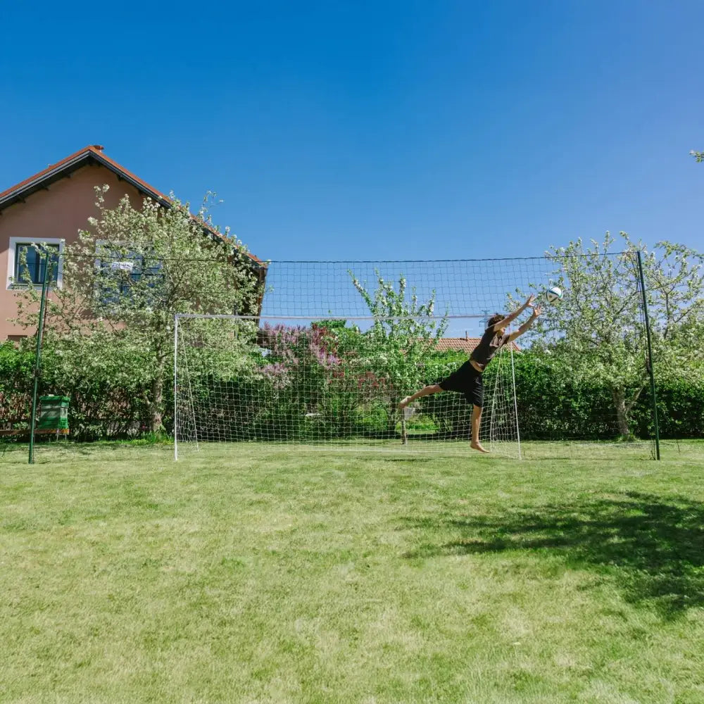 Black and white volleyball net with green poles set up in backyard for open goaaal football goal 3-in-1 trainer large