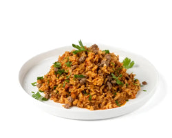 Patagonia rice pot 150g sisältää oranssinväristä riisiä paistetun jauhelihan ja tuoreen persiljan kanssa valkoisella lautasella