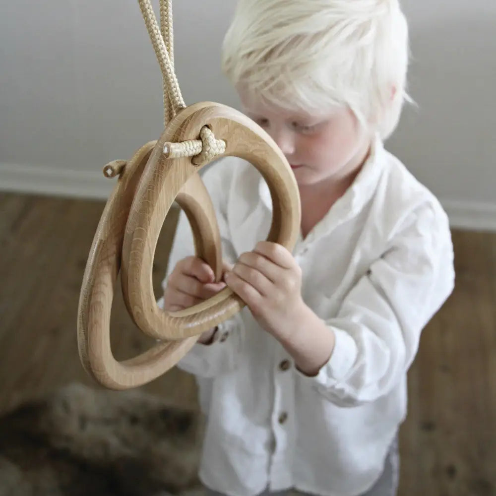 Natural-finish oak gymnastic rings with white braided rope suspension for fitness training