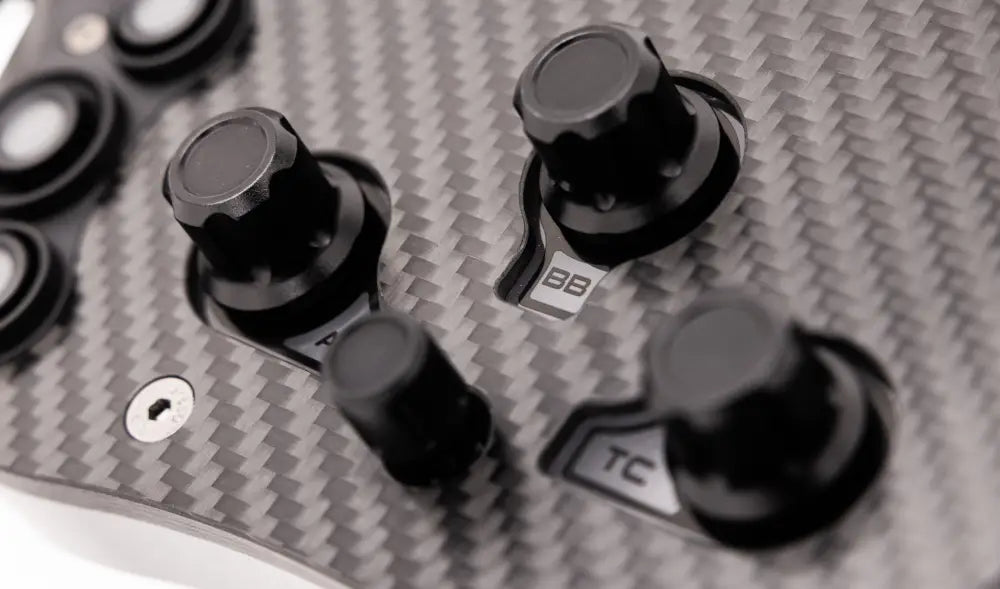 Black knurled knobs with labeled metallic bases mounted on carbon fiber panel of simagic fx-c formula steering wheel back side