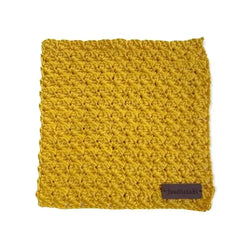 A mustard-yellow crocheted dishcloth with a textured pattern and a small brown leather tag in the corner