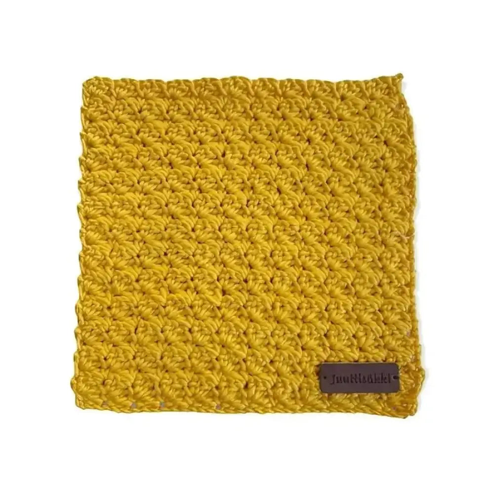 A mustard-yellow crocheted dishcloth with a textured pattern and a small brown leather tag in the corner