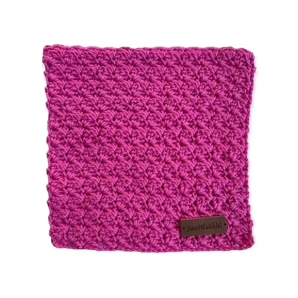 A vibrant fuchsia crocheted dishcloth with a uniform textured pattern and a small brown leather tag in one corner