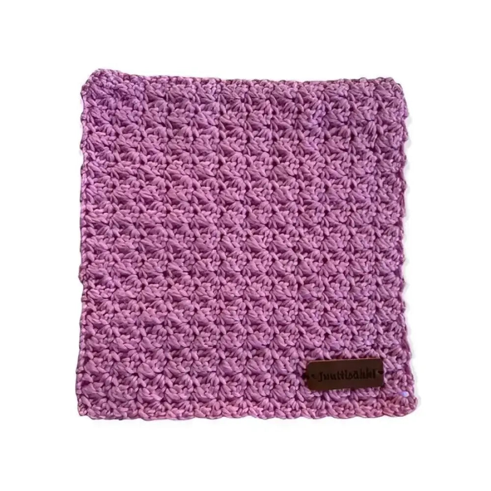 A soft lavender crocheted tiskirätti sikinsokin dishcloth with a textured pattern and a small brown leather tag