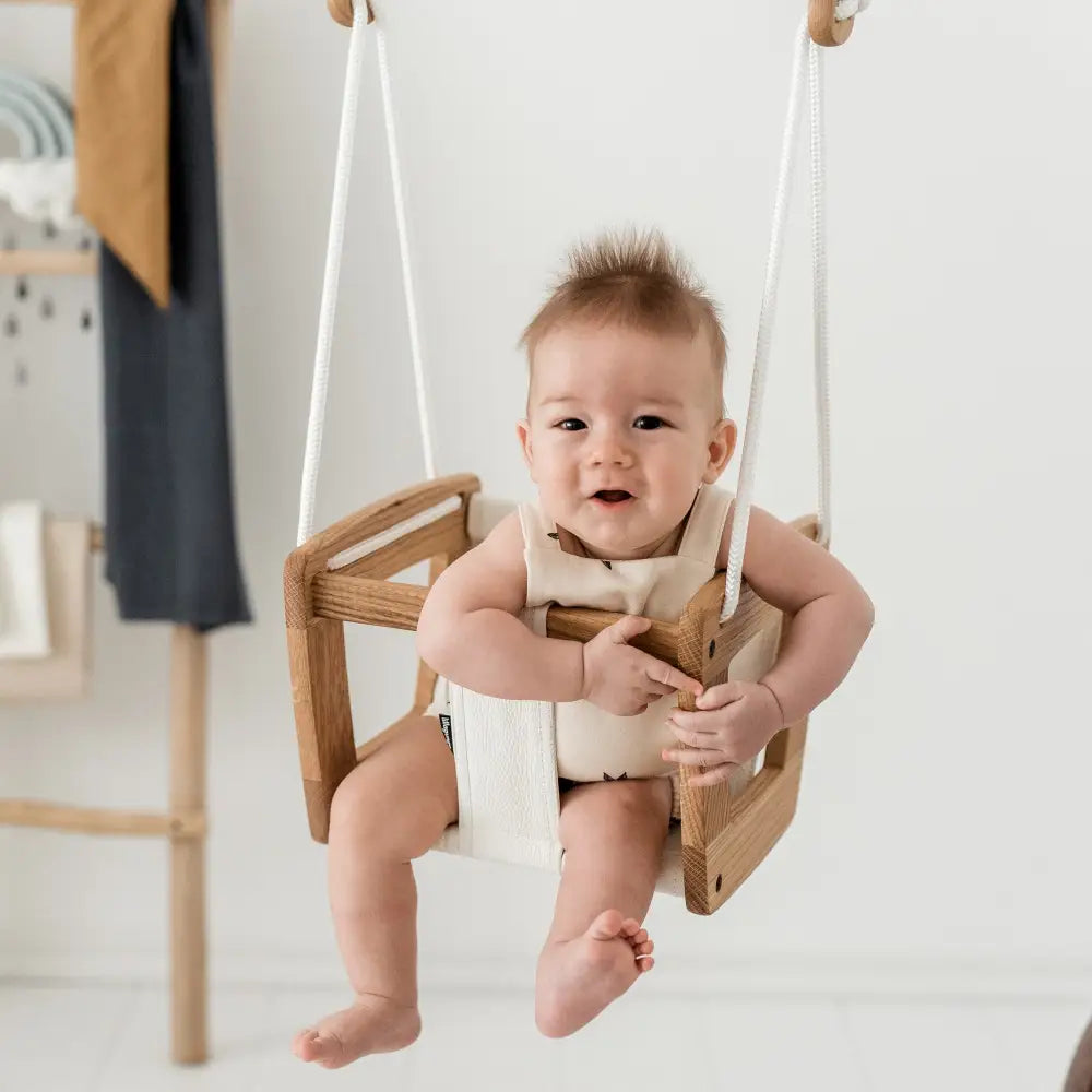 Vauvalla istutaan puisessa keinuissa, joissa on valkoiset köydet ja kerma kangasistuimessa, toddler oak musta nahka