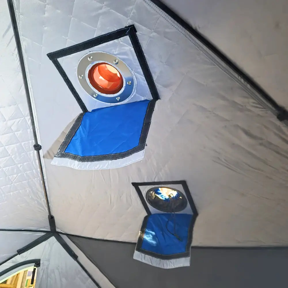 A circular orange heating element with a metallic rim installed in the ceiling of a white quilted väinö ice lodge 800 pilkkiteltta
