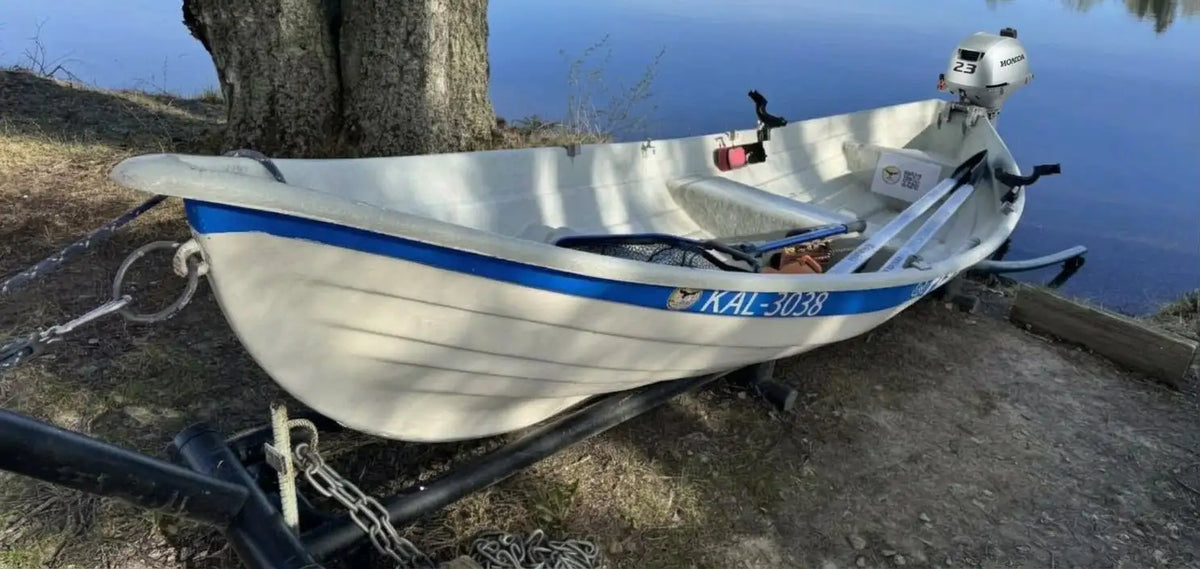 Valkoinen alumiininen kalastusvene, jossa on sininen raita ja ’kal-308’’-rekisterikilpi, varustettuna hopeanvärisellä perämoottorilla.